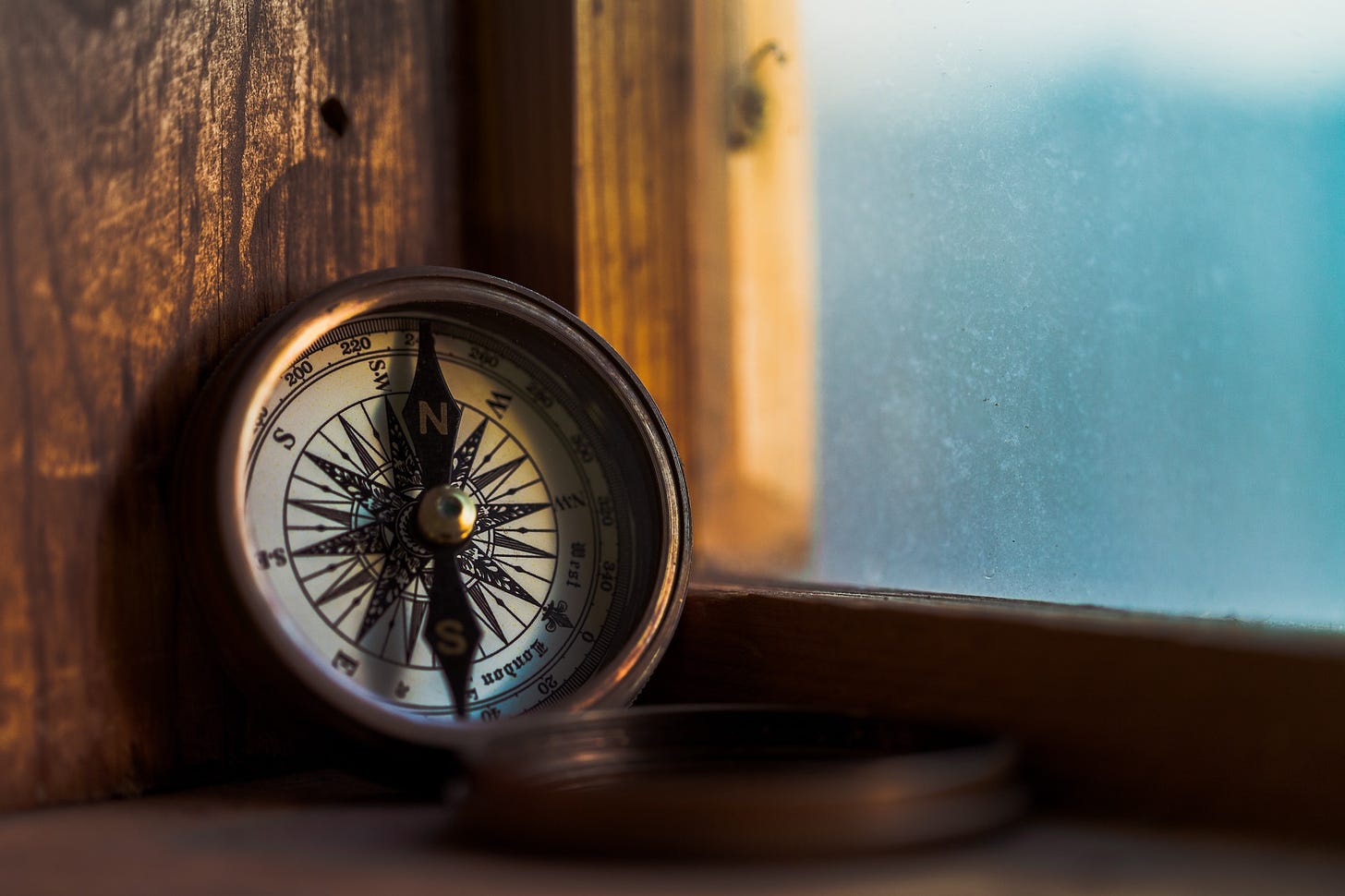 Vintage compass sitting on a window ledge with blue sea beyond.