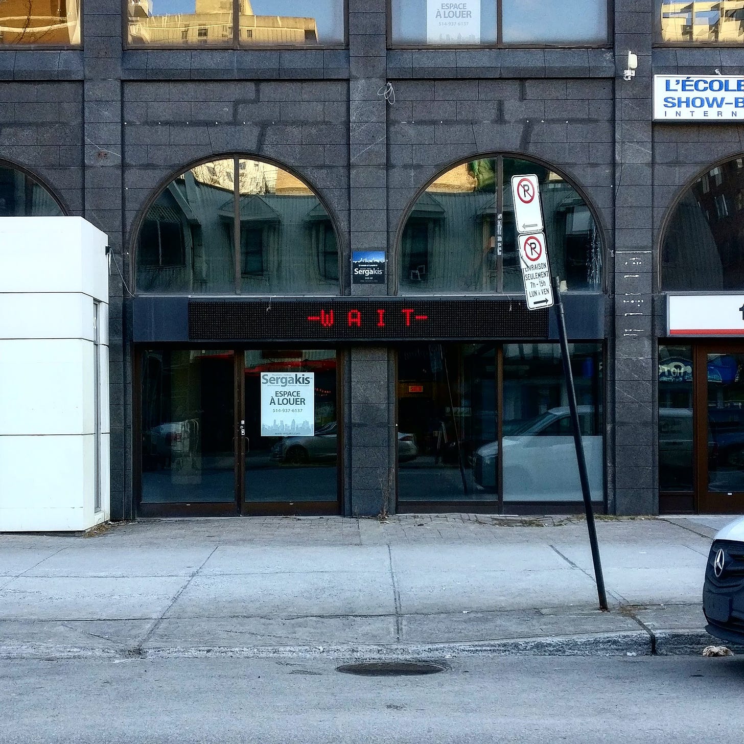 An empty storefront in Montreal with an electronic sign that says "- wait -"