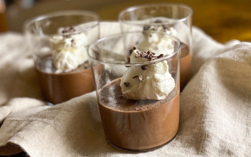 Three servings of chocolate mousse, served in glass tumblers, topped with whipped cream and cacao nibs