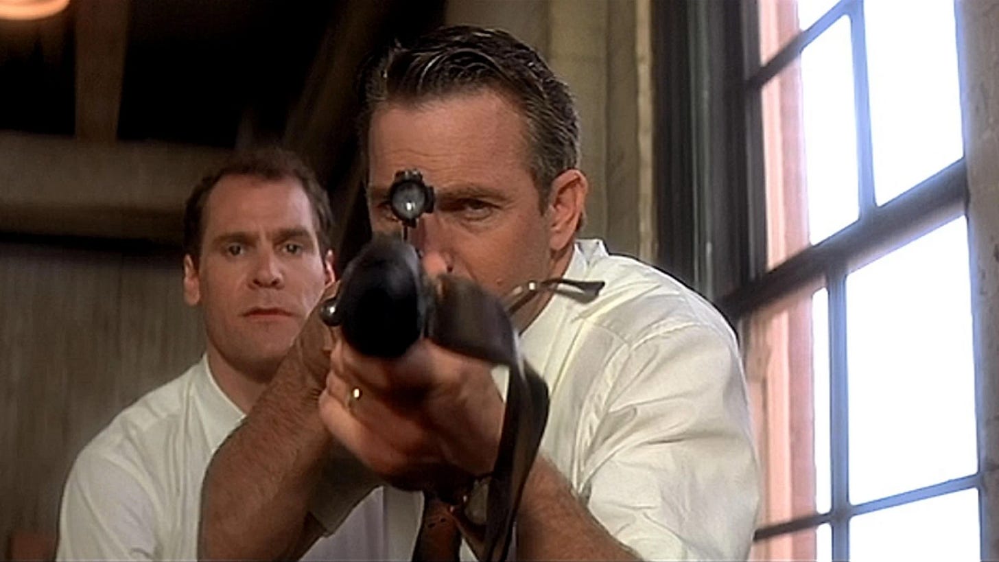 This image shows New Orleans District Attorney Jim Garrison (played by Kevin Costner) aiming a Mannlicher-Carcano rifle (like the one supposedly fired by Lee Harvey Oswald during John F. Kennedy's assassination) directly at camera. Garrison's chief investigator, Lou Ivon (played by Jay O. Sanders) is visible behind Garrison. Both men crouch in front of the same window, on the sixth floor of the Texas School Book Depository, from which Oswald supposedly shot the president. This image shows New Orleans District Attorney Jim Garrison (played by Kevin Costner) aiming a Mannlicher-Carcano rifle (like the one supposedly fired by Lee Harvey Oswald during John F. Kennedy's assassination) directly at camera. Garrison's chief investigator, Lou Ivon (played by Jay O. Sanders) is visible behind Garrison. Both men crouch in front of the same window, on the sixth floor of the Texas School Book Depository, from which Oswald supposedly shot the president.