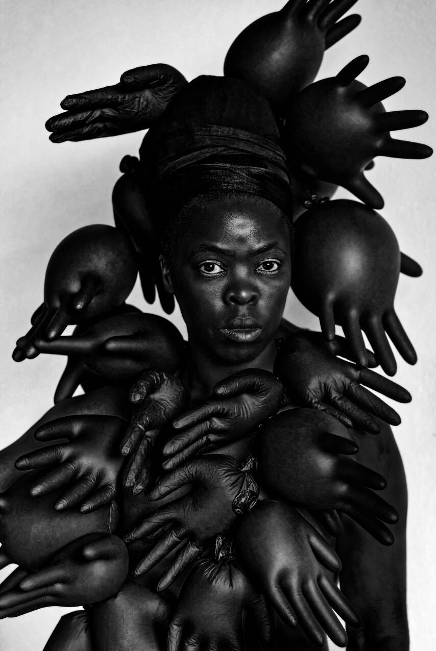 A portrait of a Black person surrounded by black protective gloves, which are filled with air.