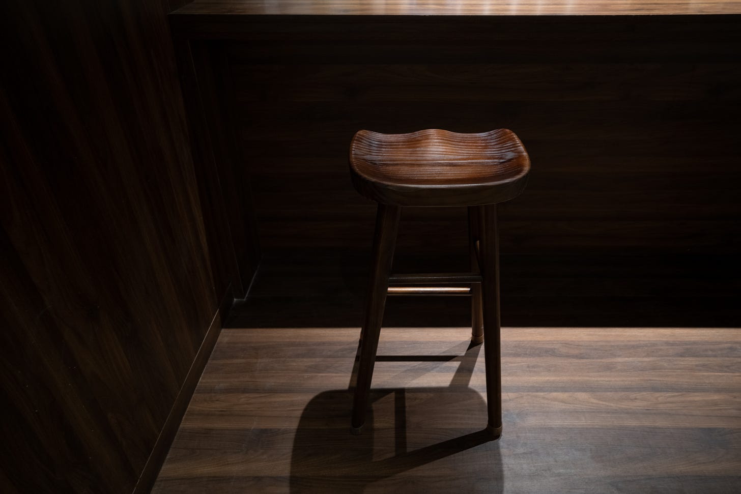 A lone wooden bar stool next to  a wooden bar on a hard wood floor