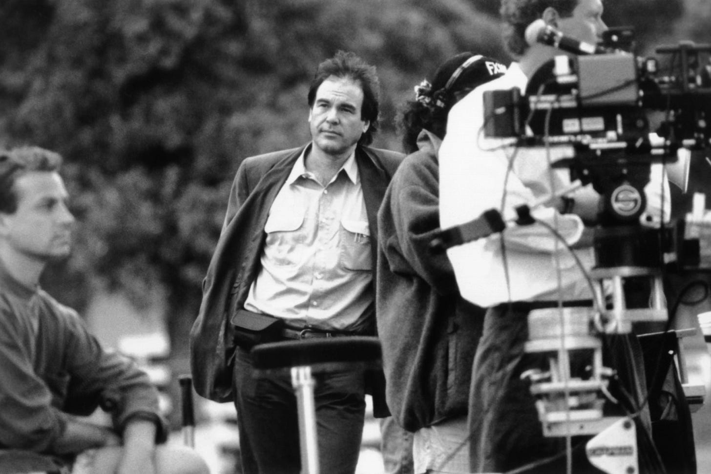 This black-and-white image shows director and co-writer Oliver Stone looking into the distance as a camera crew sets up a shot in his 1991 film JFK. This black-and-white image shows director and co-writer Oliver Stone looking into the distance as a camera crew sets up a shot in his 1991 film JFK.