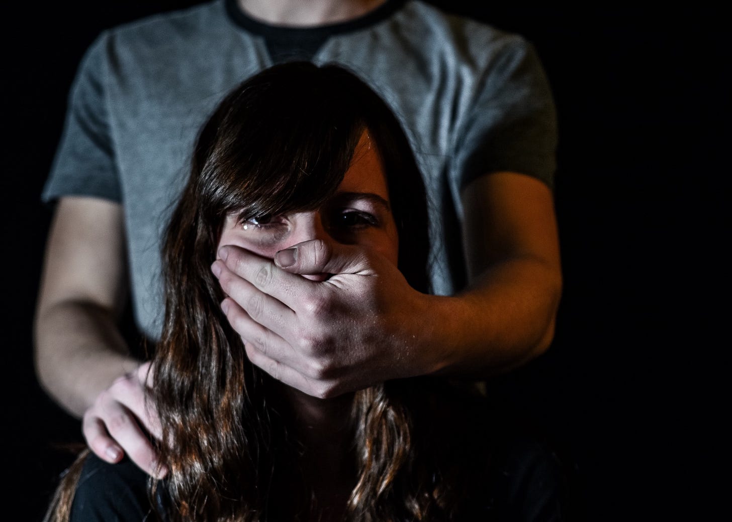 A woman cries silently as her partner covers her mouth forcefully with his hand from behind.
