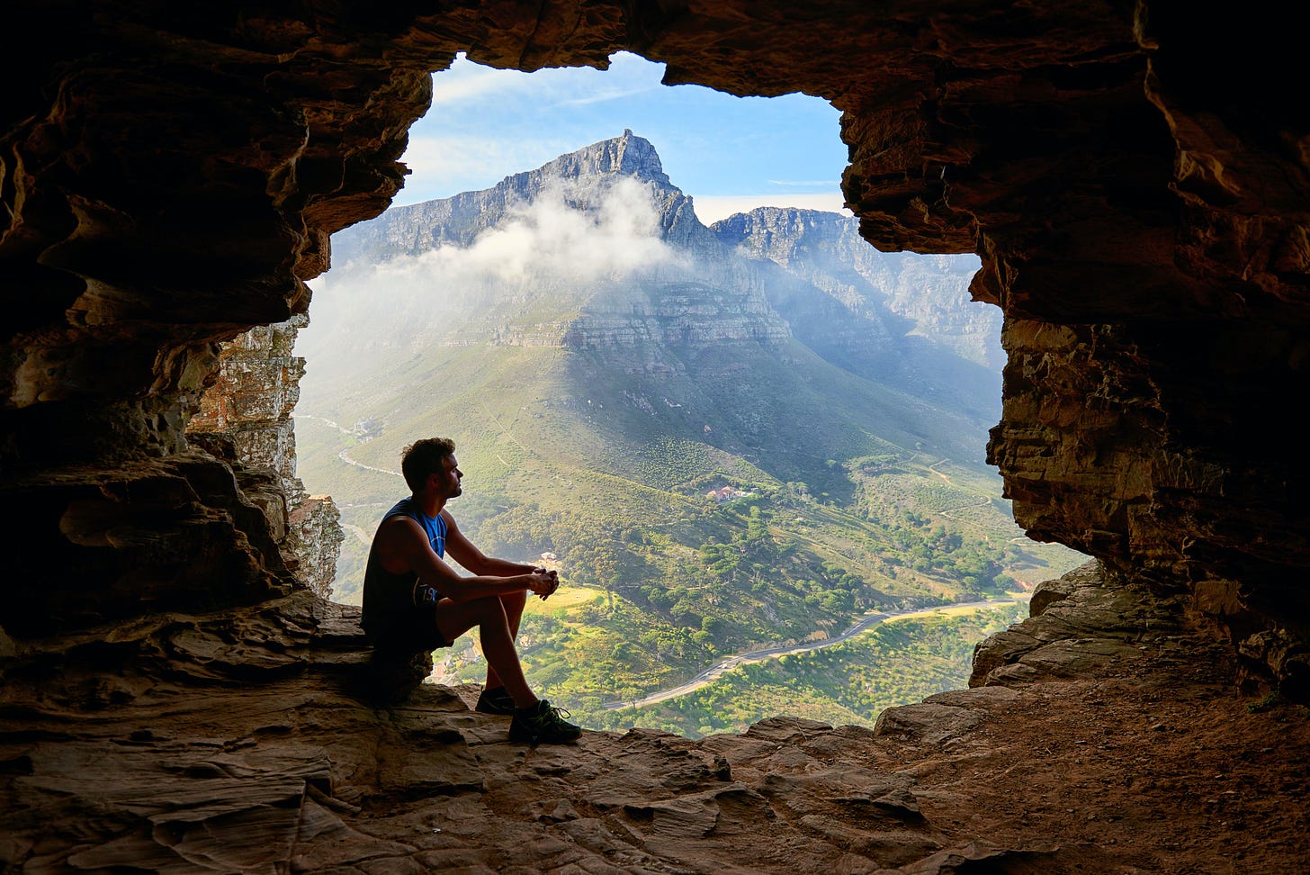 A man sitting inside a cave overlooking a mountain.