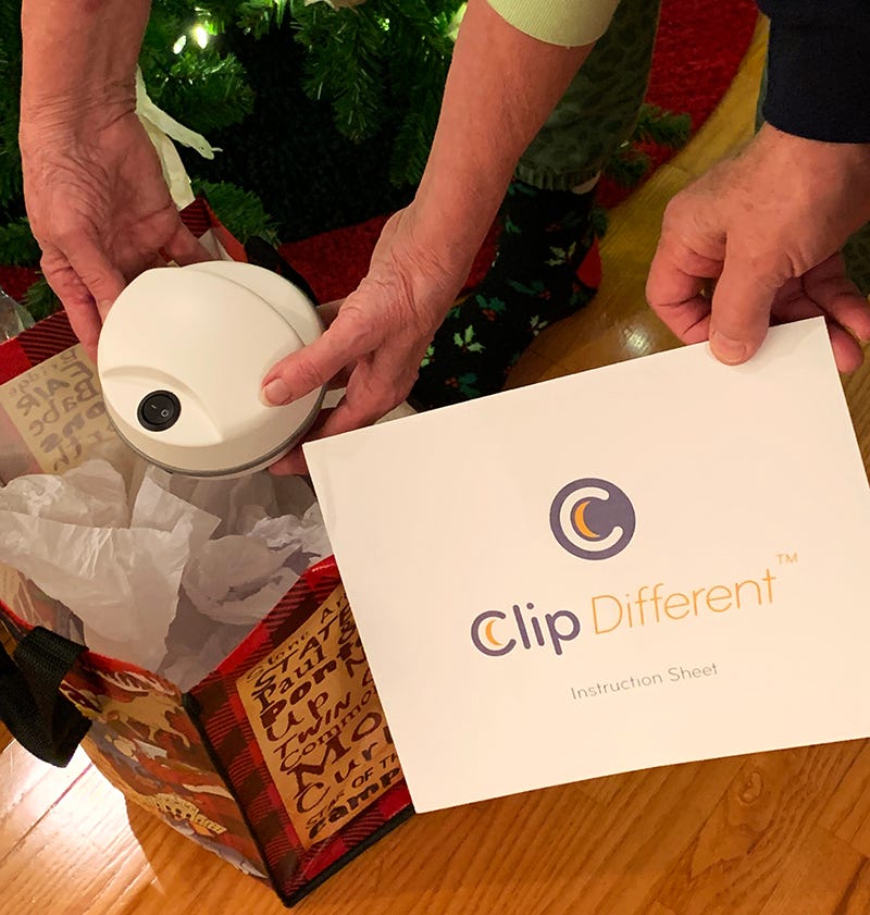 Two pairs of hands, one holding the ClipDifferent the other holding the ClipDifferent instruction sheet after unwrapping a Christmas gift in front of a Christmas tree.