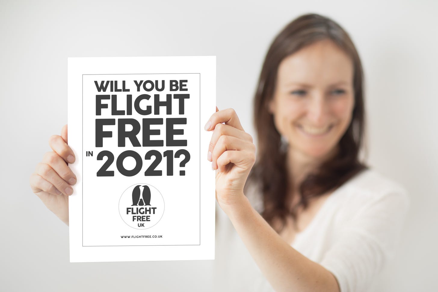 A smiling woman holds a sign that says 'Will you be flight free in 2021?'
