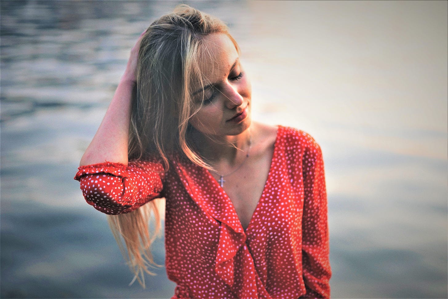 pensive girl with blonde hair wearing red and white polka dot top watery background