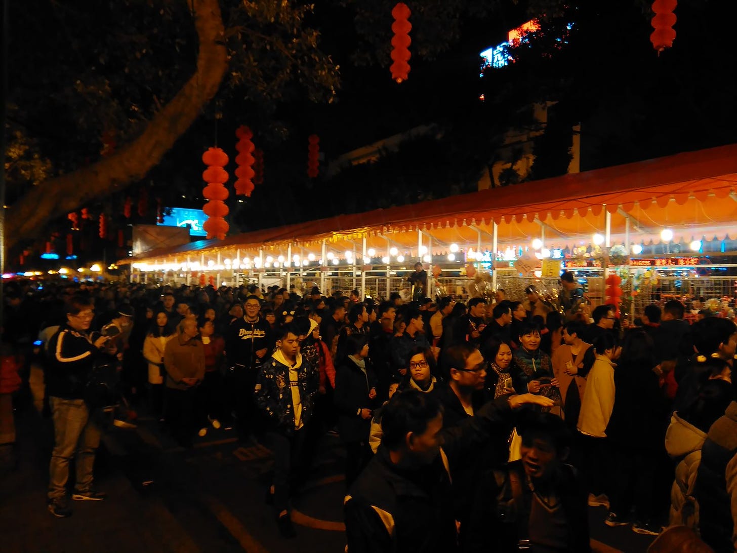 A very crowded night market in Guangzhou, lit by hanging Chinese red lanterns and electric lighting strung across the market stalls