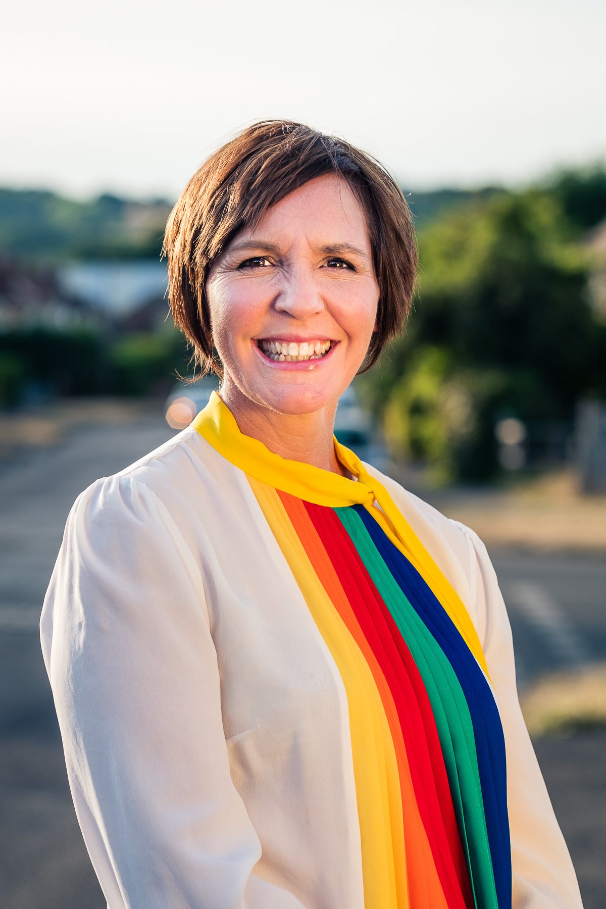 Portrait of a smiling woman wearing a white blouse with rainbow pattern outside during golden hour