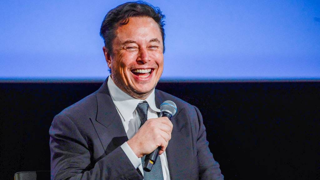 Elon Musk smiling while holding a microphone
