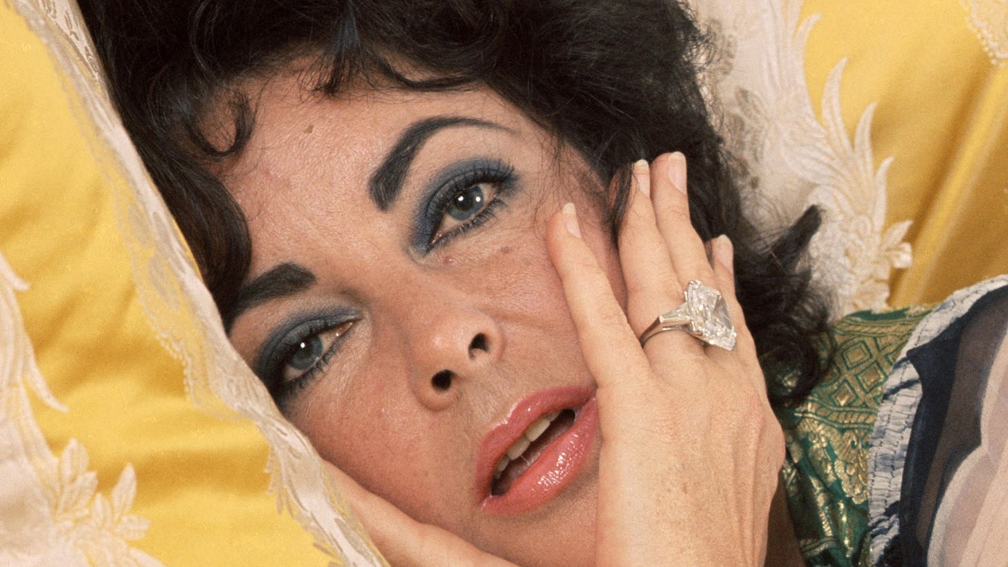 Elizabeth Taylor reclining on lemon silk with big fat diamond ring on her wedding finger