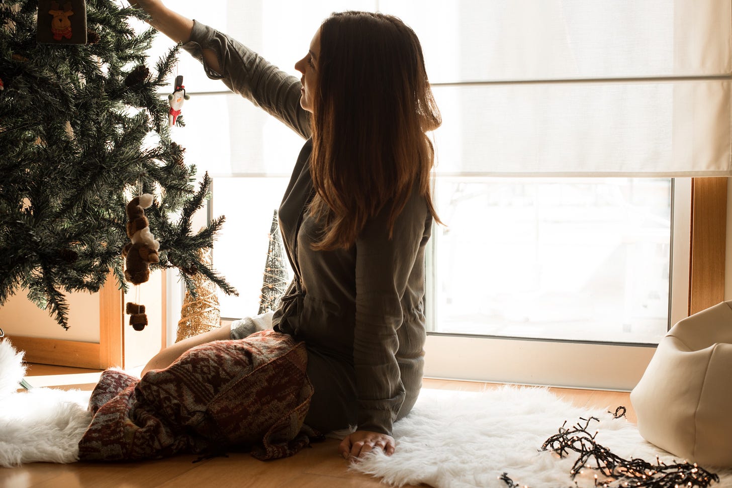 A woman happily decorates a Christmas tree on her own.