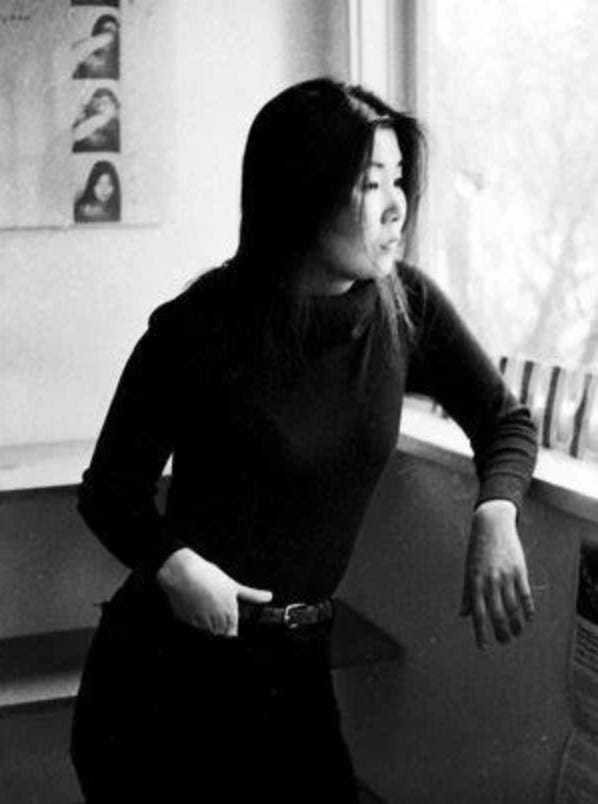 Photograph of Theresa Hak Kyung Cha. She is mainly in profile as she looks out through the window. 