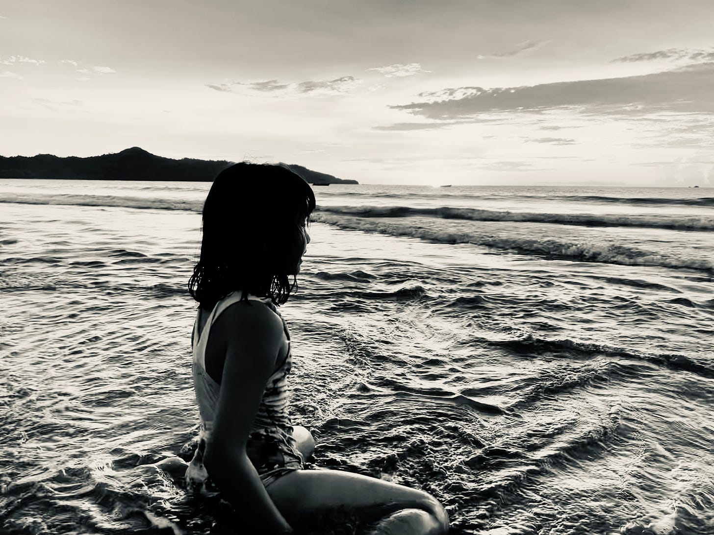 black and white photo of girl sitting in water on beach