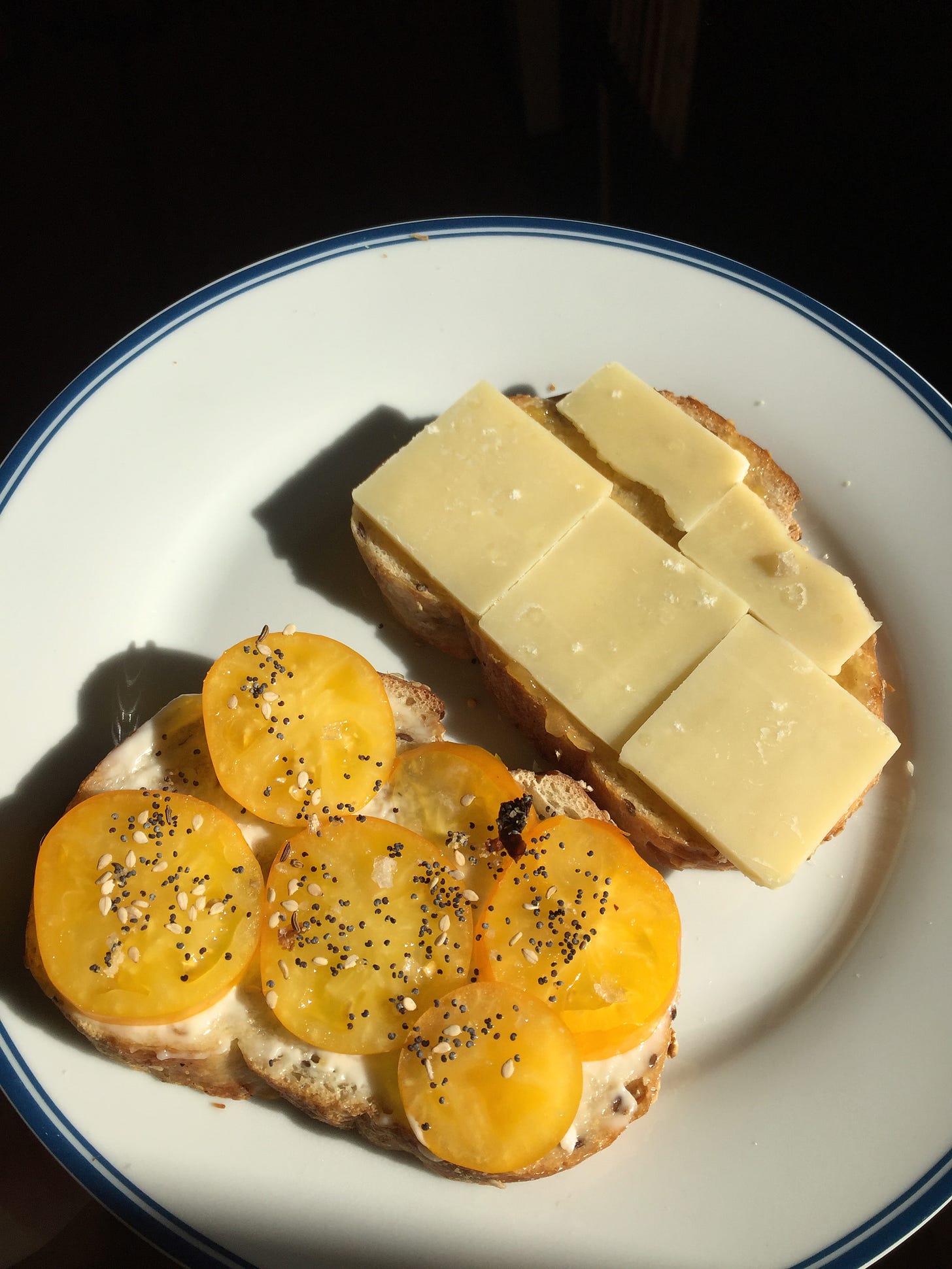 two toasts on a white plate, one with yellow heirloom tomatoes sprinkled with everything bagel seasoning, the other with peach jam and slices of gruyère cheese.