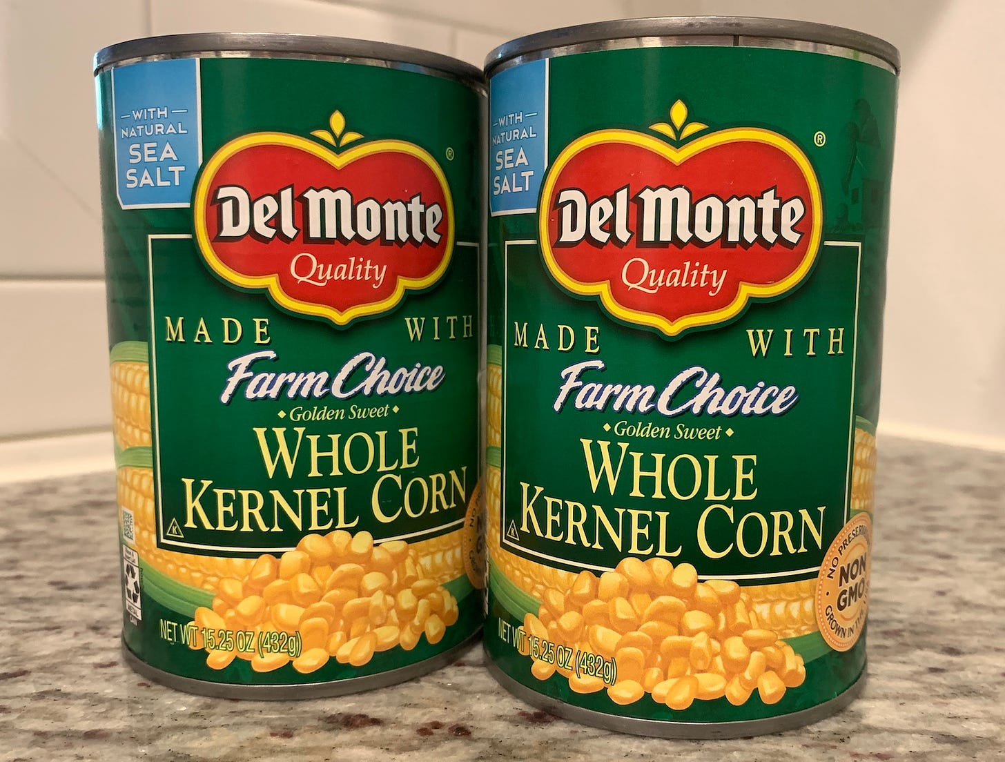 Two cans of Del Monte whole kernel corn sitting on a granite countertop