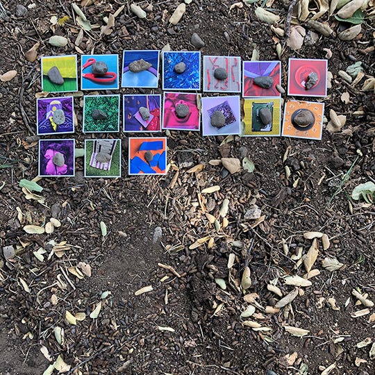 A still photo of seventeen Rainbow Squared cards laid out in a grid under an oak tree amidst California hills.