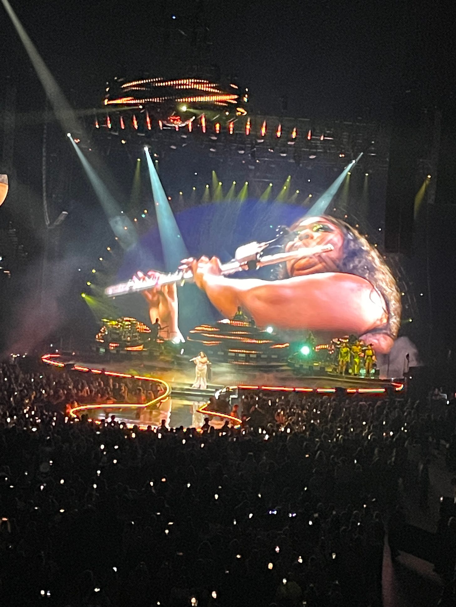Lizzo playing flute, with image of herself projected on large screen behind stage