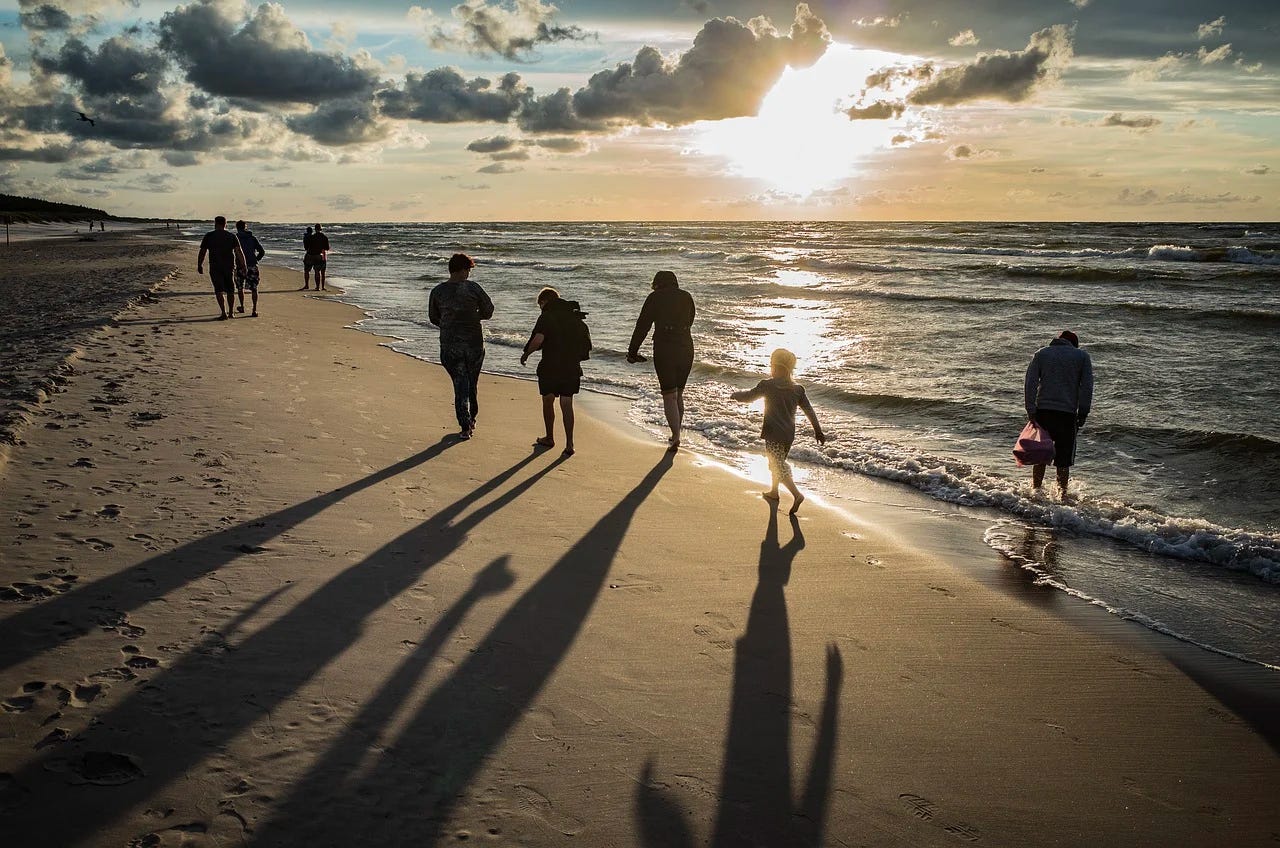 group of people spread out walking on beach at sunset