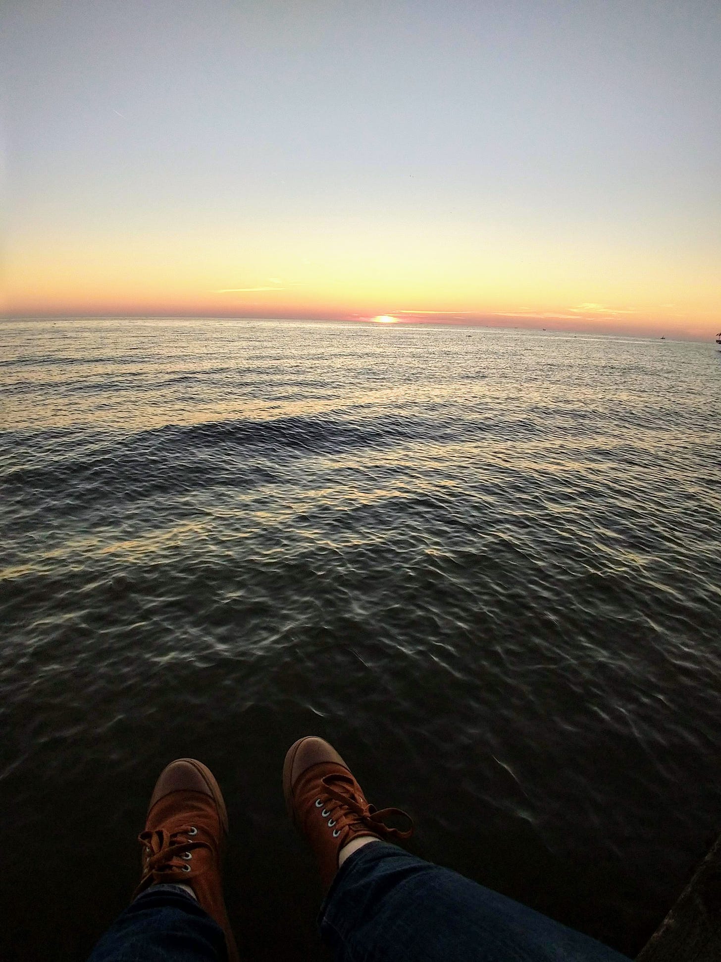 hanging my converse-style shoes over a wall I'm sitting on, the ocean in front of me as the sun dips below the horizon. While beautiful, it's a little sketchy that I'm sitting on the edge. 