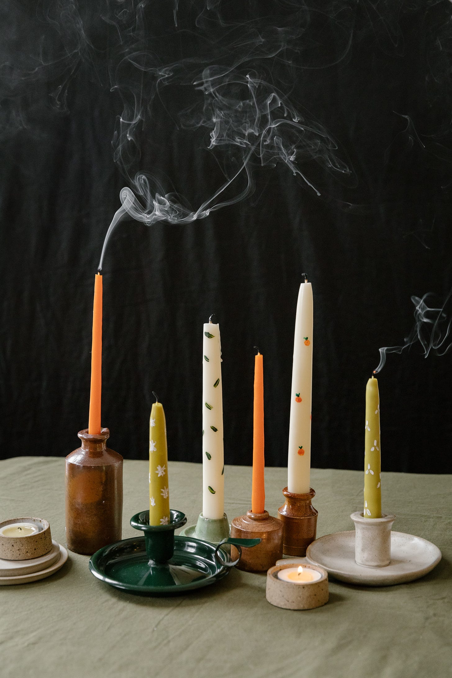 A group of tall dinner candles on a table. They are all smokey as they have just been blown out.