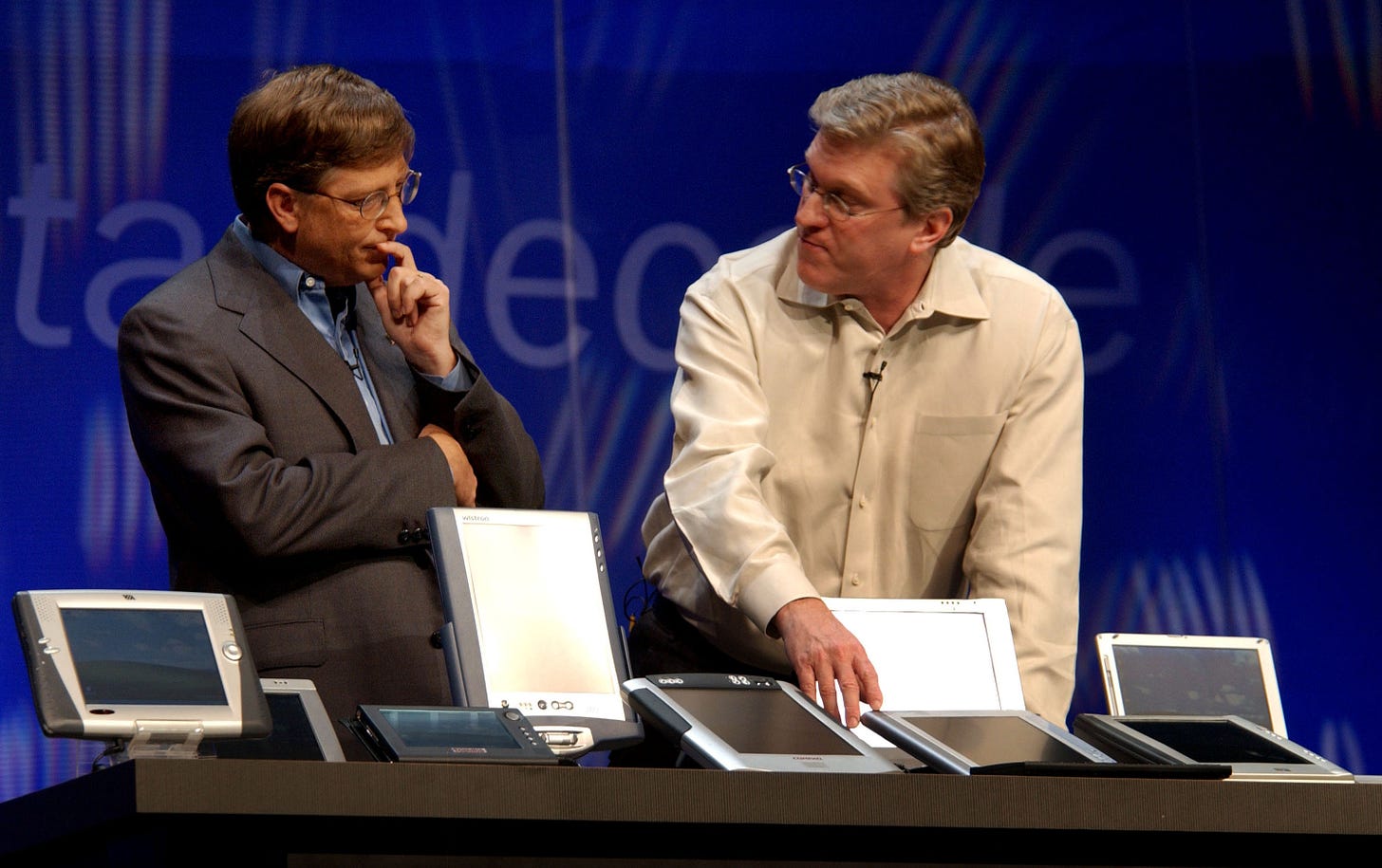 Bill Gates and Jeff Raikes on stage at Comdex 2001 looking at a collection of Windows PCs designed for Windows XP Tablet Edition.