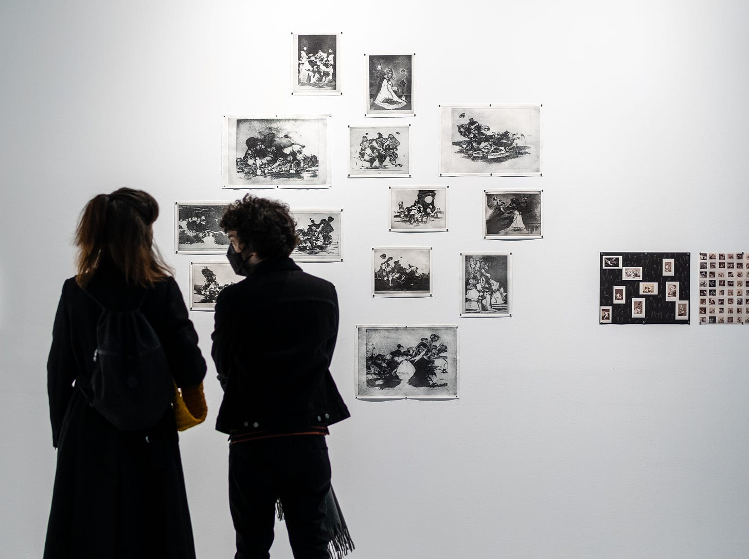 Gallery view of intaglio prints on the wall. Two people stand and chat in front of the prints, masks on.