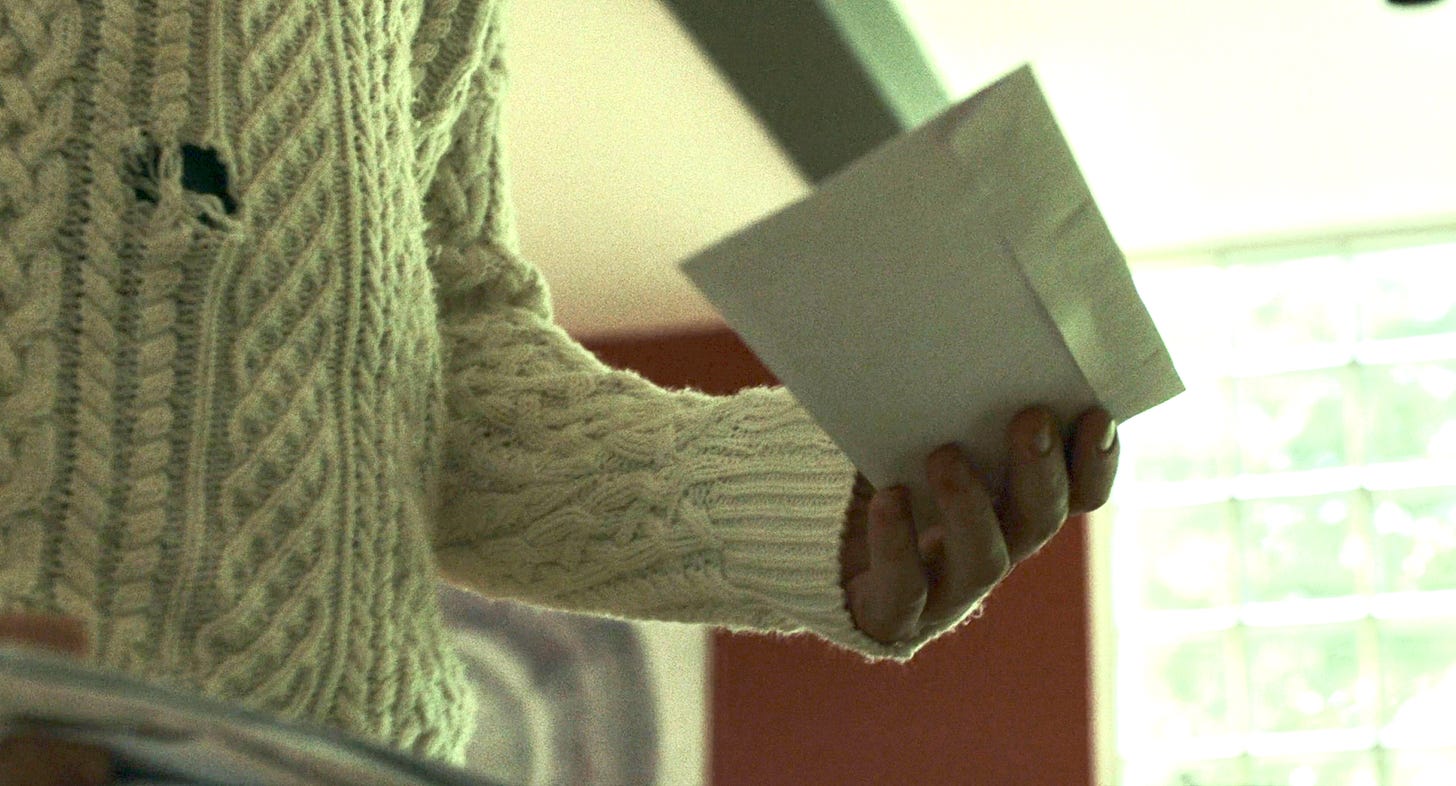 A close-up of Ransom Drysdale's distressed white Aran sweater in KNIVES OUT. He's holding an envelope.