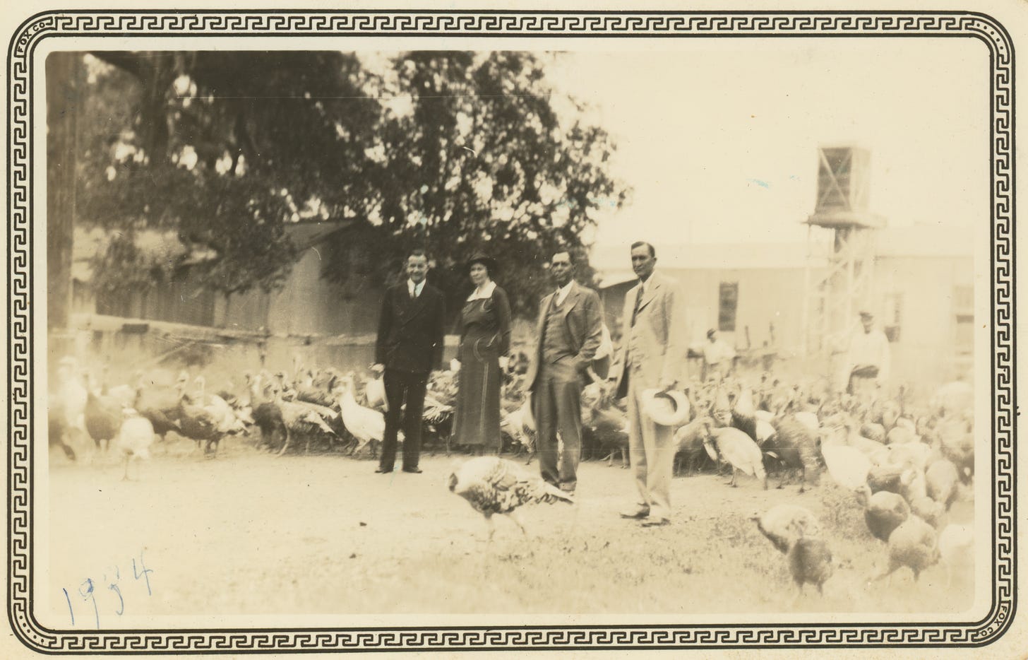 A sepia-tinted black-and-white photo of three men in suits and a woman in a dress, standing amid a flock of turkeys