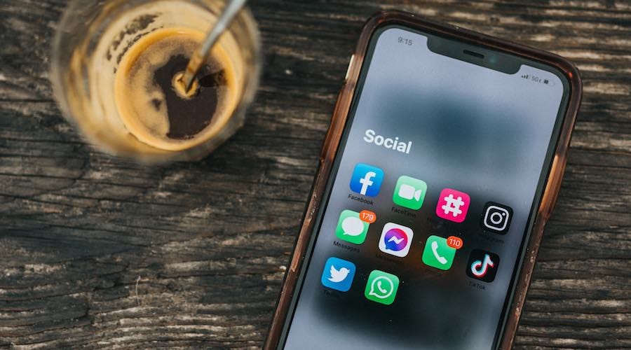 Social media app icons on iPhone on table next to coffee drink