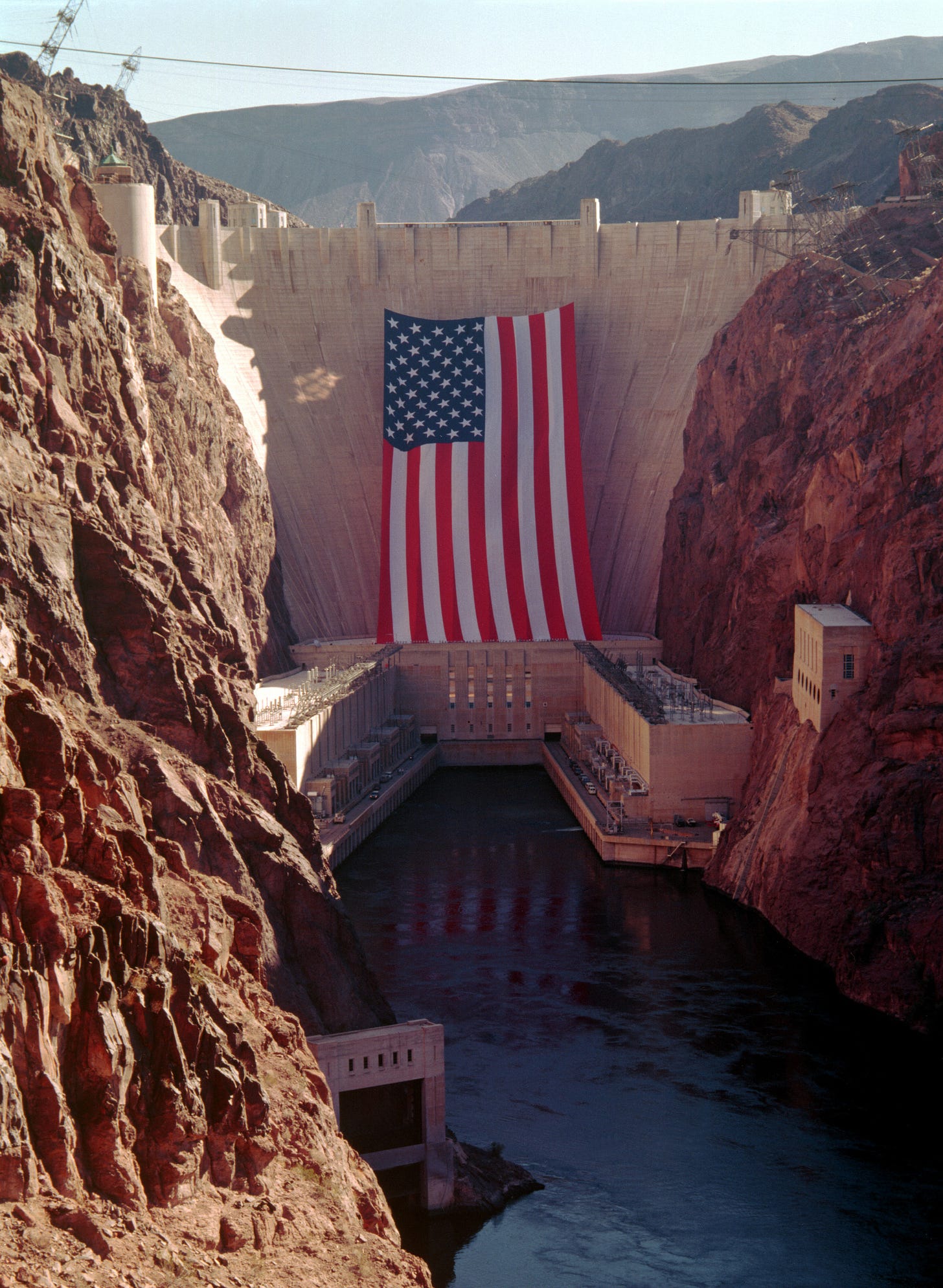 Photo of the Hoover Dam with a massive American flag attached to its downstream face. The flag was hoisted onto the dam for the 1996 Summer Olympics: The torch traveled across on its way to Atlanta, Georgia,
