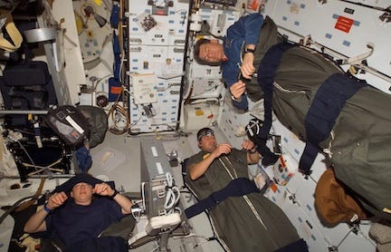 Three astronauts strapped into sleeping bags, sleeping upright in a space shuttle.