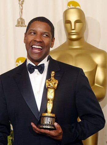 Imagem do ator negro Denzel Washington vestido de terno e gravata borboleta segurando uma estatueta do Oscar