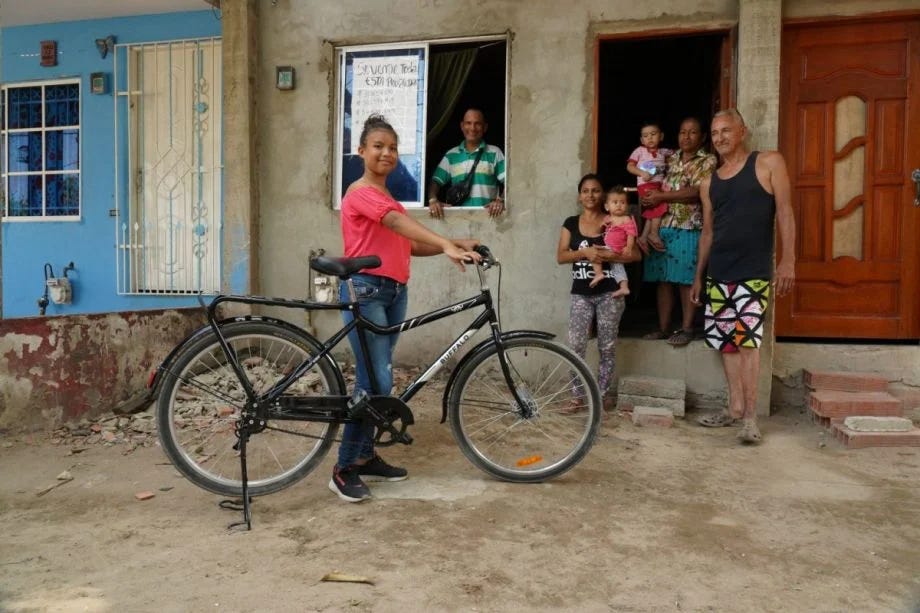 young woman with bicycle in front of building with family members.  She looks confident and all are happy.