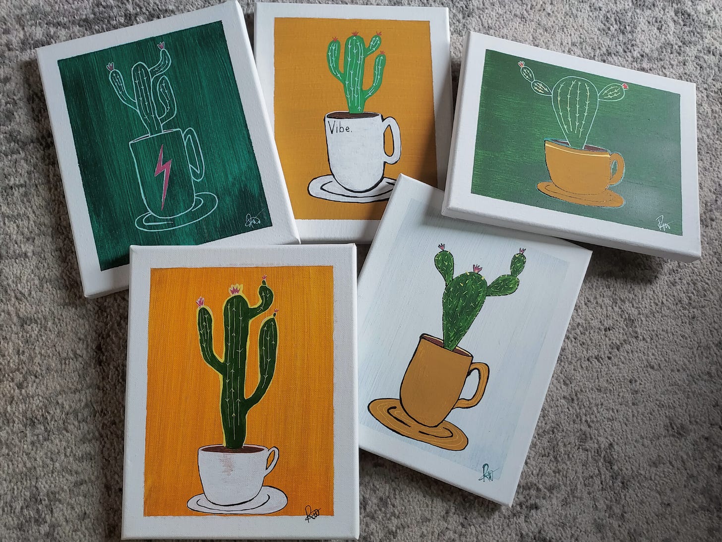 A wide shot of five paintings on the ground. They are poorly painted cactus coming out of coffee mugs in various colors of mustard, white, and green.