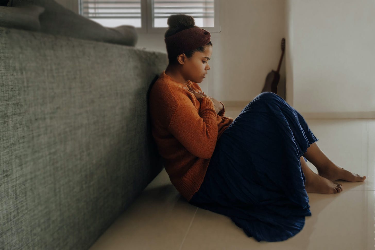 A young person sits behind a couch, holding her hands to her chest and looking worried.