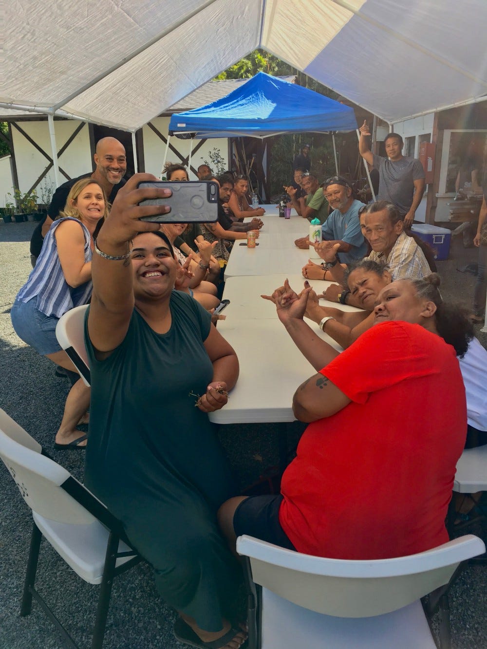 A group of people pose for a selfie around a table, throwing shakas.