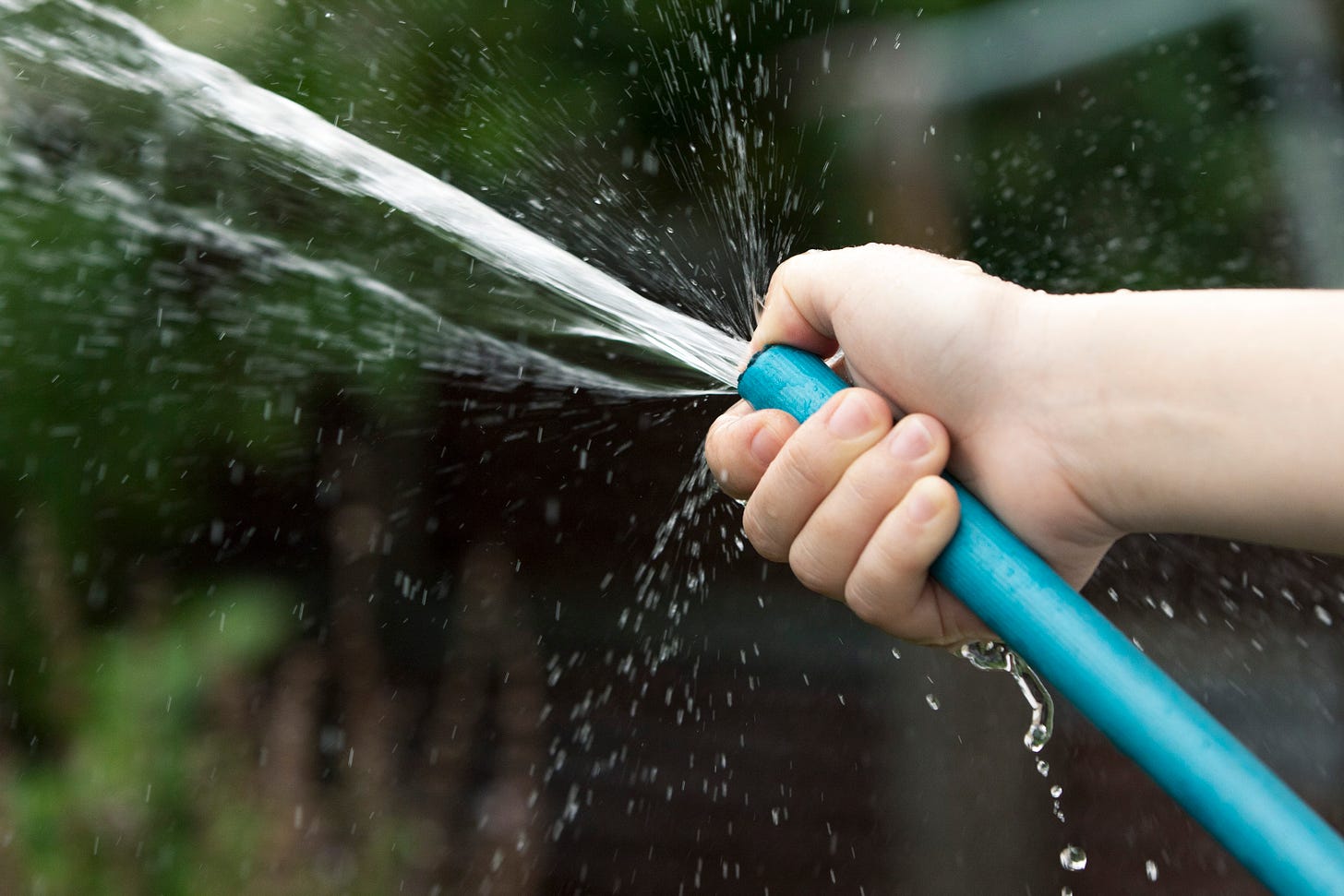 A hand holding a blue hose and using their thumb to make the water spray faster