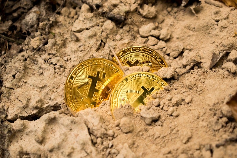 Three golden bitcoins buried in the sand.