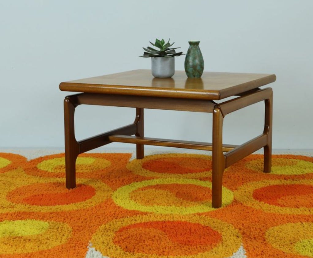 a 70s teak coffee table with clean, smooth lines. it's on a gorgeous, groovy orange and yellow geometric rug.