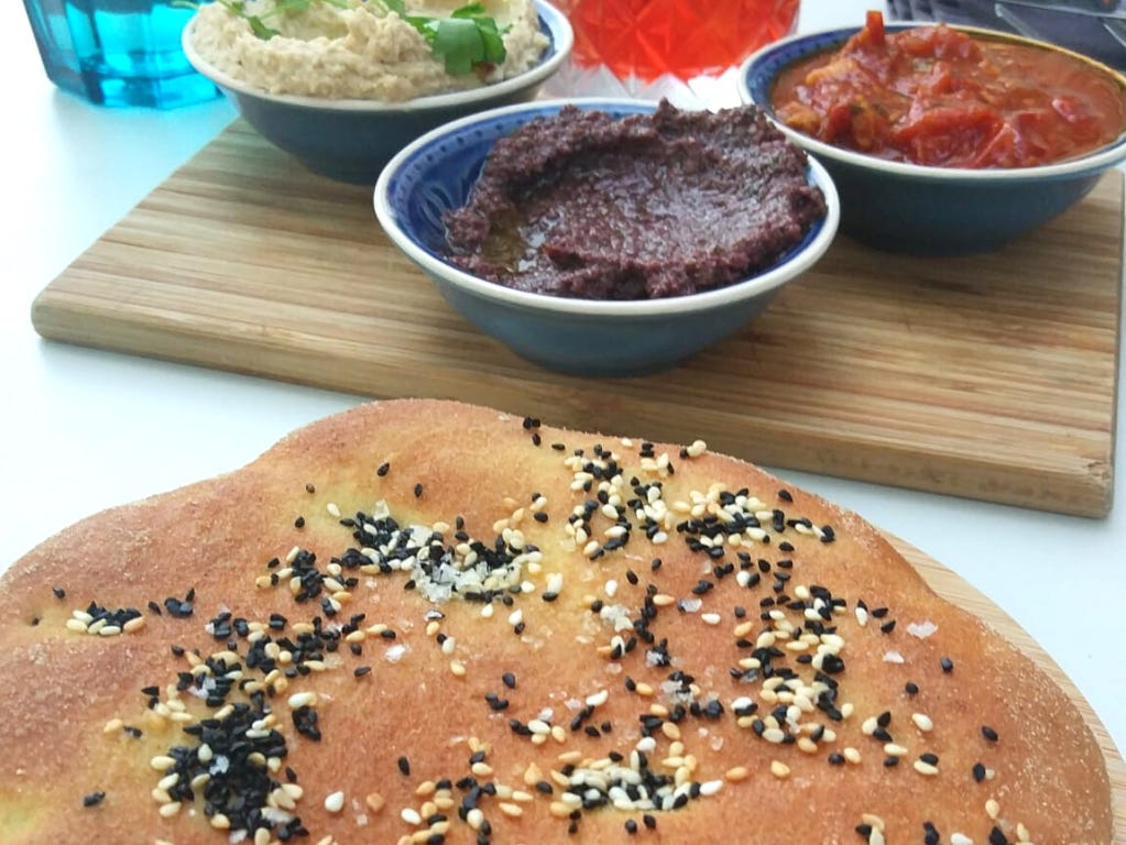 Moroccan khobz, a type of round bread, topped with nigella seeds and served with three dips