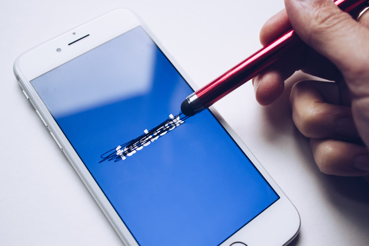 Photo of a pen crossing out the Facebook logo on a smartphone. (Unsplash)