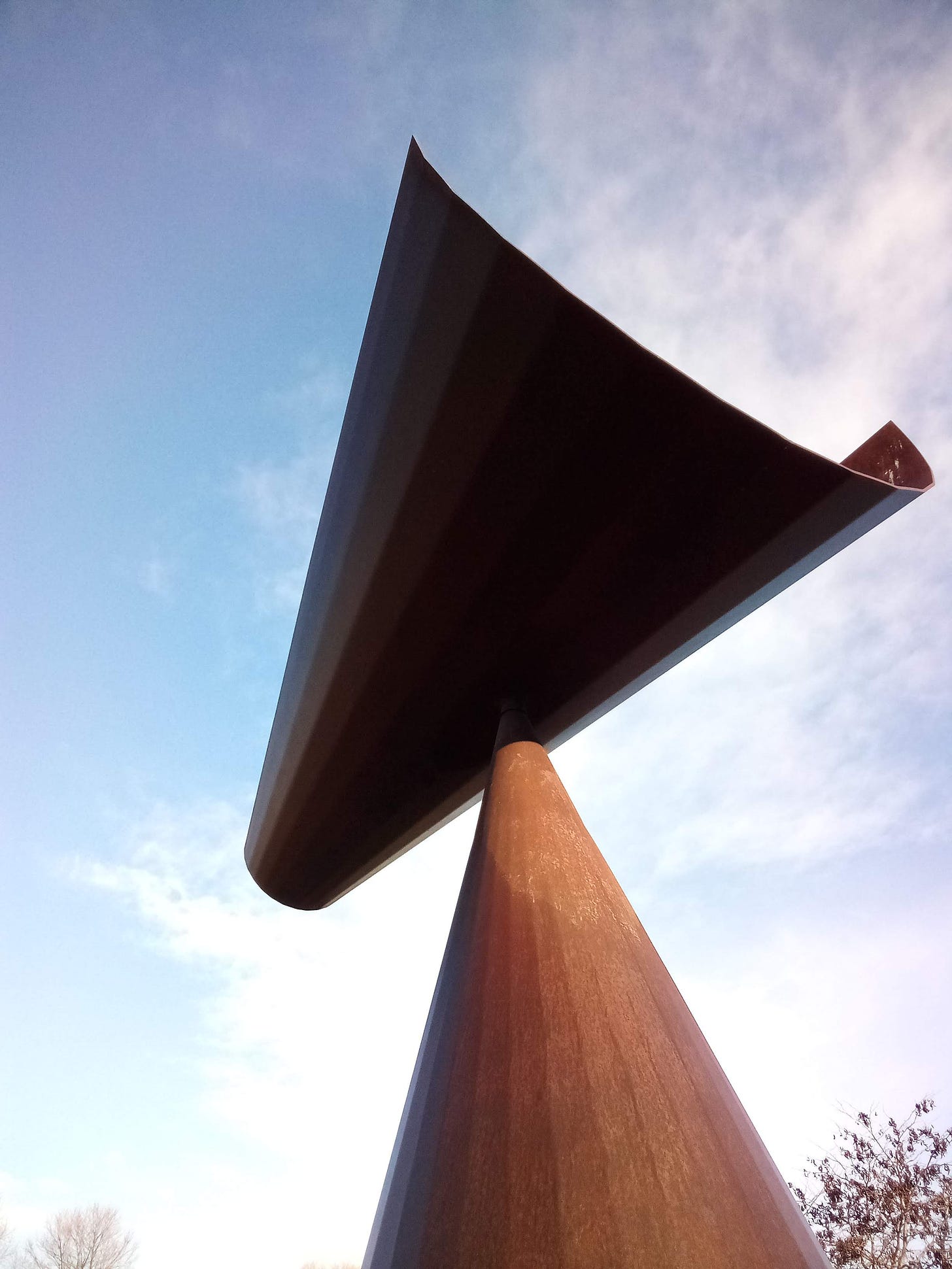 Bronze funnel wind sculpture against blue sky and clouds