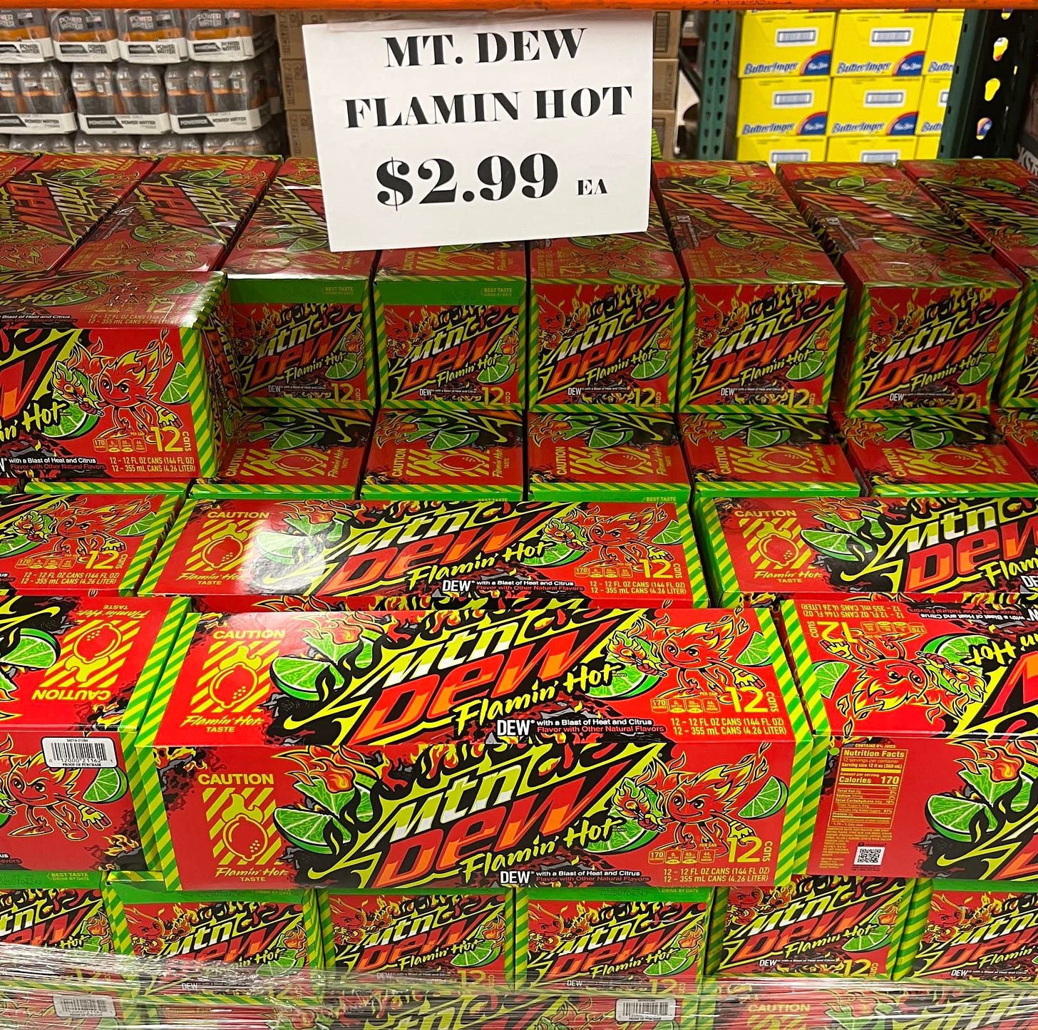 bright green and orange twelve packs of mountain dew flamin hot, stacked ten across and eight high, with a sign up top reading mt. dew flamin hot $2.99 each
