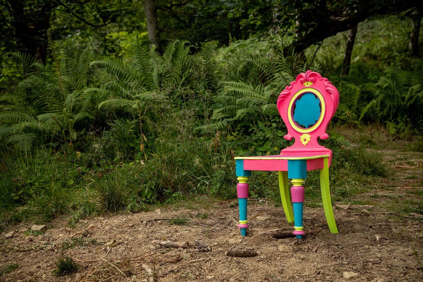 An antique chair painted in vibrant neon colours surrounded by woodland and ferns
