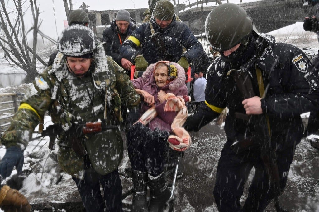 Ukrainian soldiers help an elderly woman cross a destroyed bridge as she evacuates Irpin.