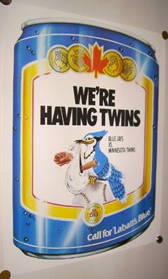 An image depicts a Blue Jay bird holding an opposing baseball player in a blanket in its beak like a stork. The tag line says "WE'RE HAVING TWINS!"