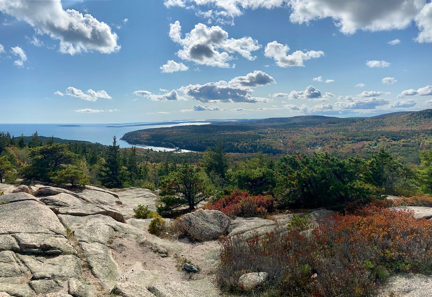Granite mountaintop looking out onto autumn-colored forests, the ocean, and a river in sunshine