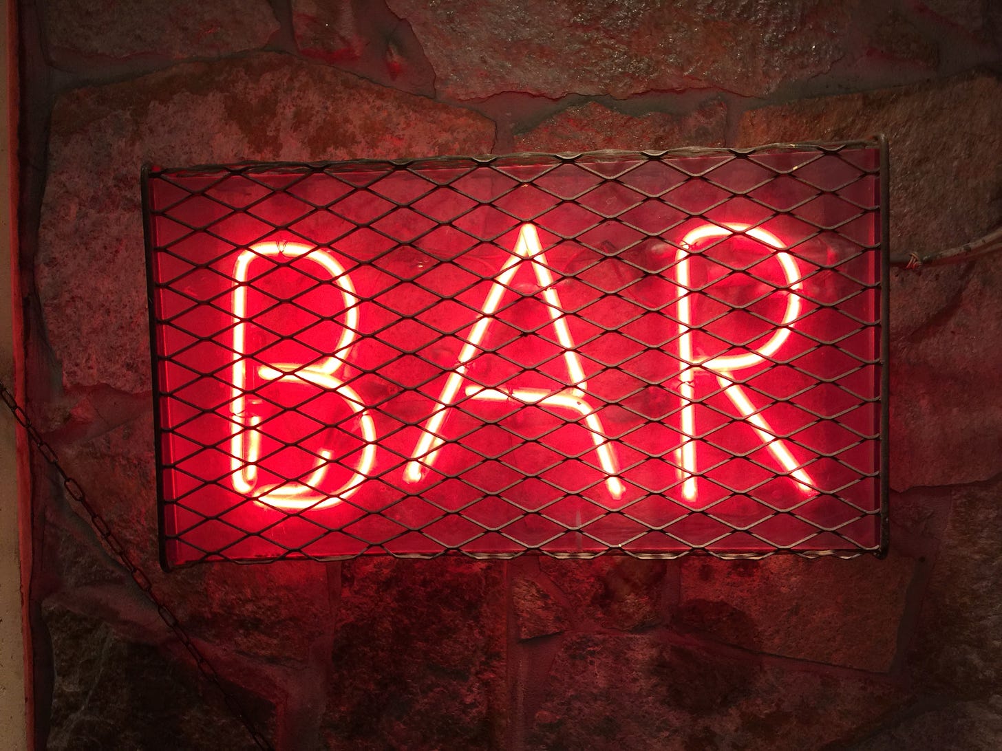 Red neon sign that says "bar" is on a wall behind a protective cage